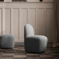Textured gray upholstered chair with a rounded back, set against a neutral-toned wall and patterned floor.