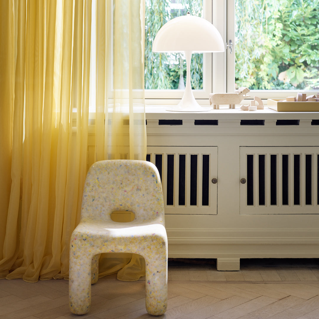"Colorful speckled chair in neutral tones with soft yellow curtains and a bright white lamp."