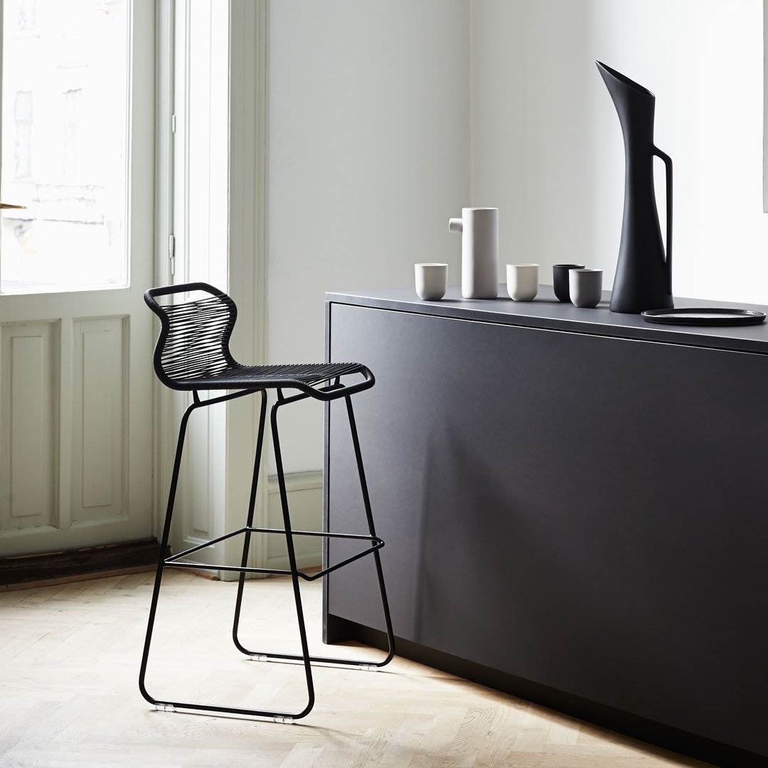 Black wire bar stool against a minimalist dark gray cabinet, featuring sleek lines and modern design.