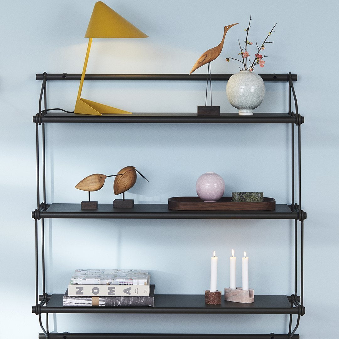 Black multi-tiered shelf with geometric patterns, yellow lamp, and decorative items in soft pastels and metallics.