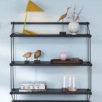 Black multi-tiered shelf with geometric patterns, yellow lamp, and decorative items in soft pastels and metallics.
