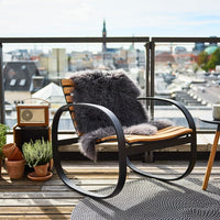 Stylish rocking chair with a gray fur throw, wooden accents, and textured round rug, set against a city backdrop.