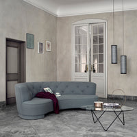 Light gray curved sofa with tufted upholstery, accented by a burgundy throw and minimalist glass coffee table.