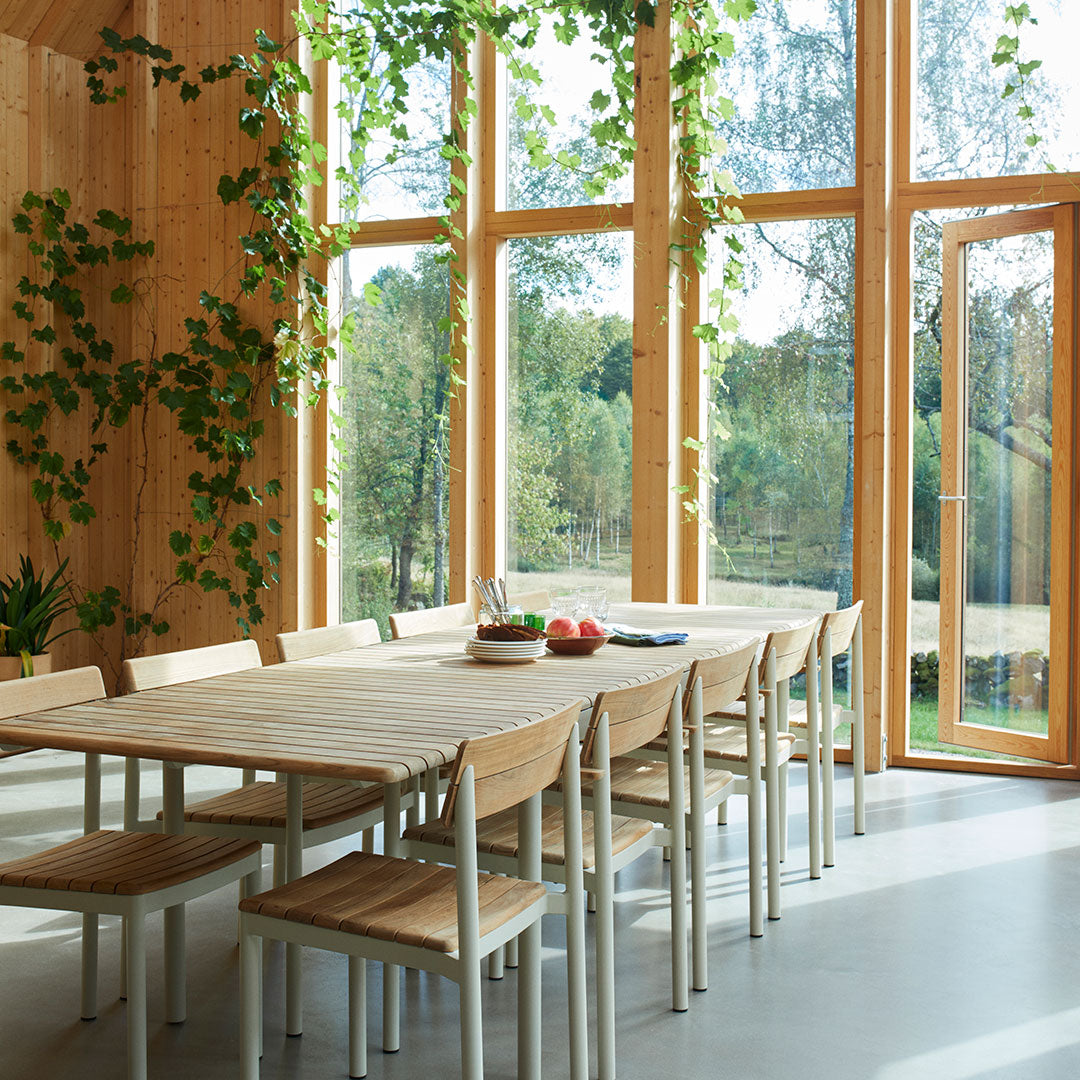 Wooden dining table with natural tones, light grey chairs, and vibrant green foliage creating a fresh, inviting atmosphere.