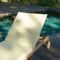 Cream-colored lounge chair with a smooth fabric on a wooden deck near a sparkling blue pool.