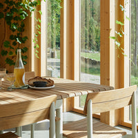 Light wood dining table with natural tones, complemented by green ivy and a serene outdoor backdrop.