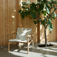 Neutral beige chair with light wood accents against a warm wooden backdrop and lush green foliage.