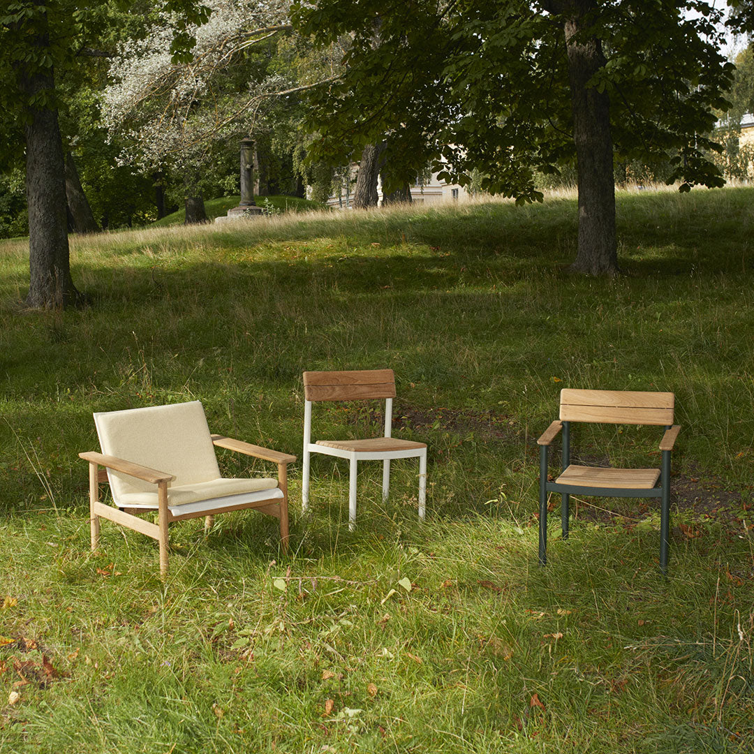 Three outdoor chairs: beige fabric, white and wood, dark green metal with wooden accents on a grassy field.