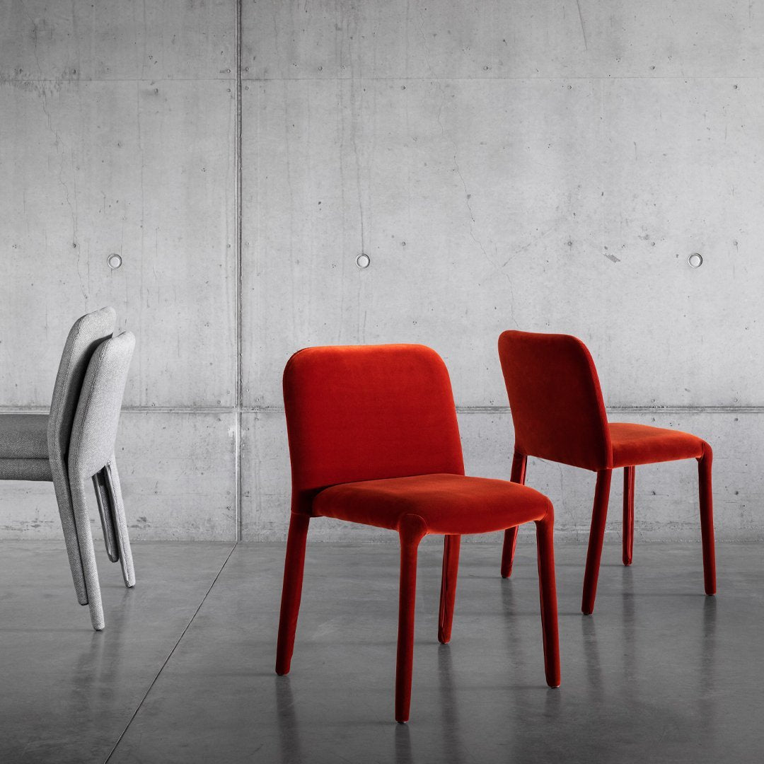 "Set of modern chairs in vibrant red and soft gray velvet against a sleek concrete backdrop."