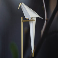 Elegant white origami bird sculpture with a sleek gold stand, set against a dark background for striking contrast.