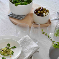 Elegant white dinnerware with a neutral cloth, accented by green salad and wooden serving tray, showcasing a modern dining setup.