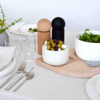 White bowl with olives, black and beige salt shakers, green salad in a bowl, neutral table setting with subtle patterns.