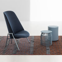 Blue patterned chair on a vibrant orange and grey woven rug, accented by light blue side tables.
