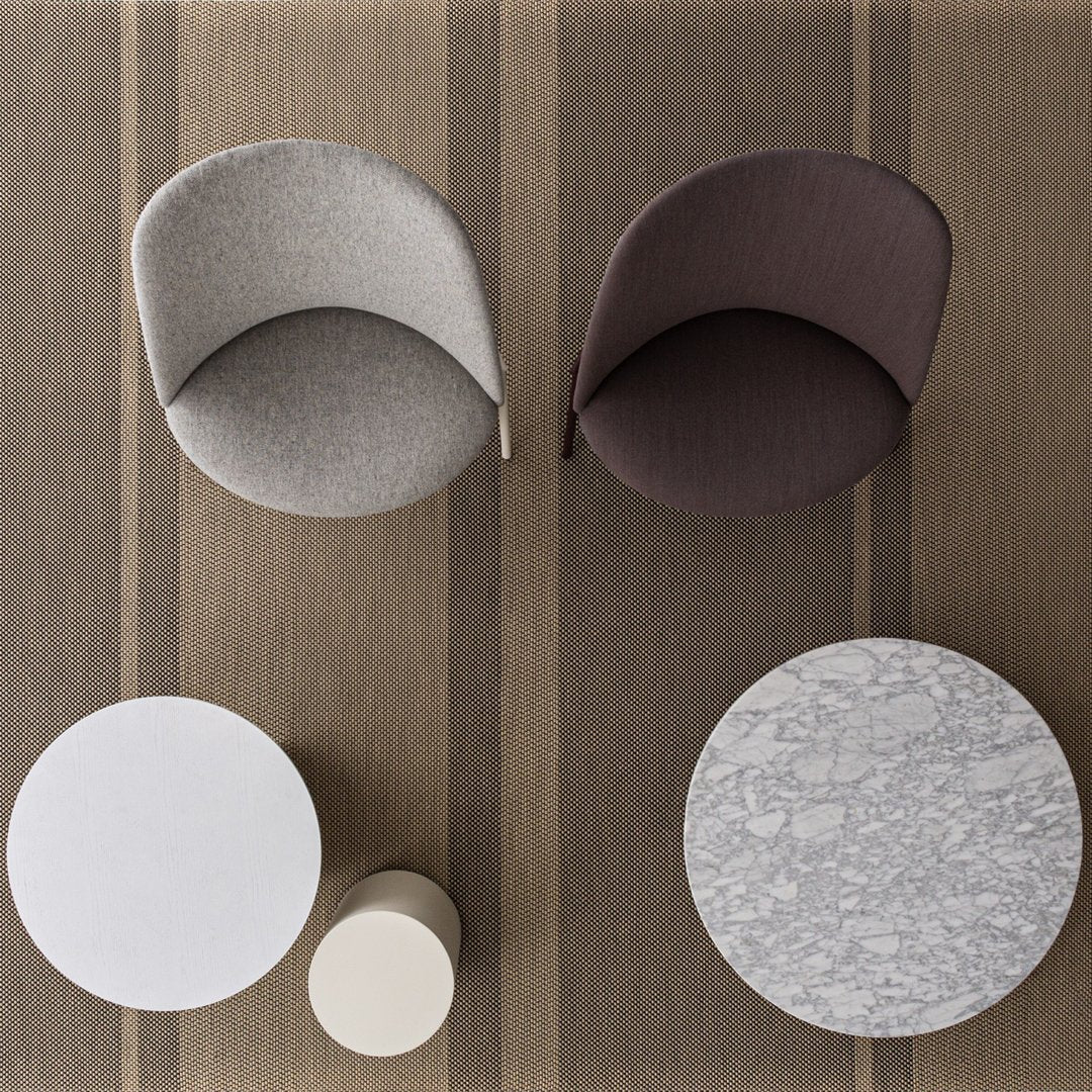 Two stylish chairs in grey and brown, alongside white and round patterned tables on a striped brown rug.