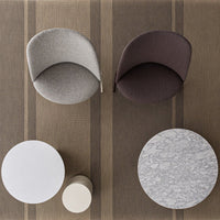 Two stylish chairs in grey and brown, alongside white and round patterned tables on a striped brown rug.