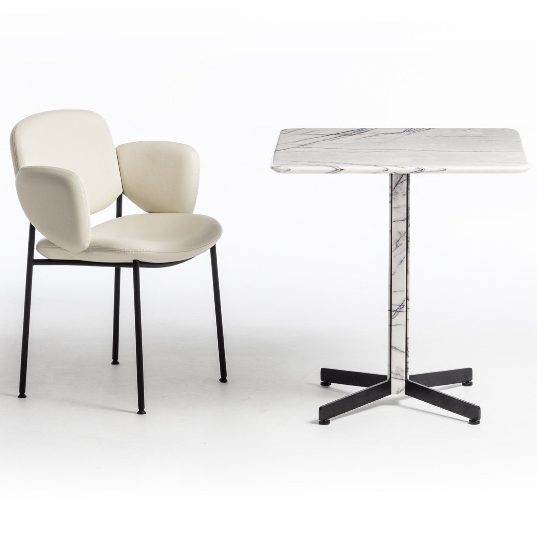 Cream upholstered chair with black legs beside a white marble top table featuring a gray veining pattern.