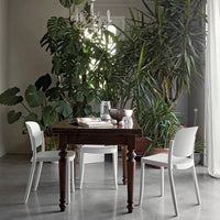 "Elegant dark wood table with white chairs, surrounded by lush green plants in a bright, airy room."