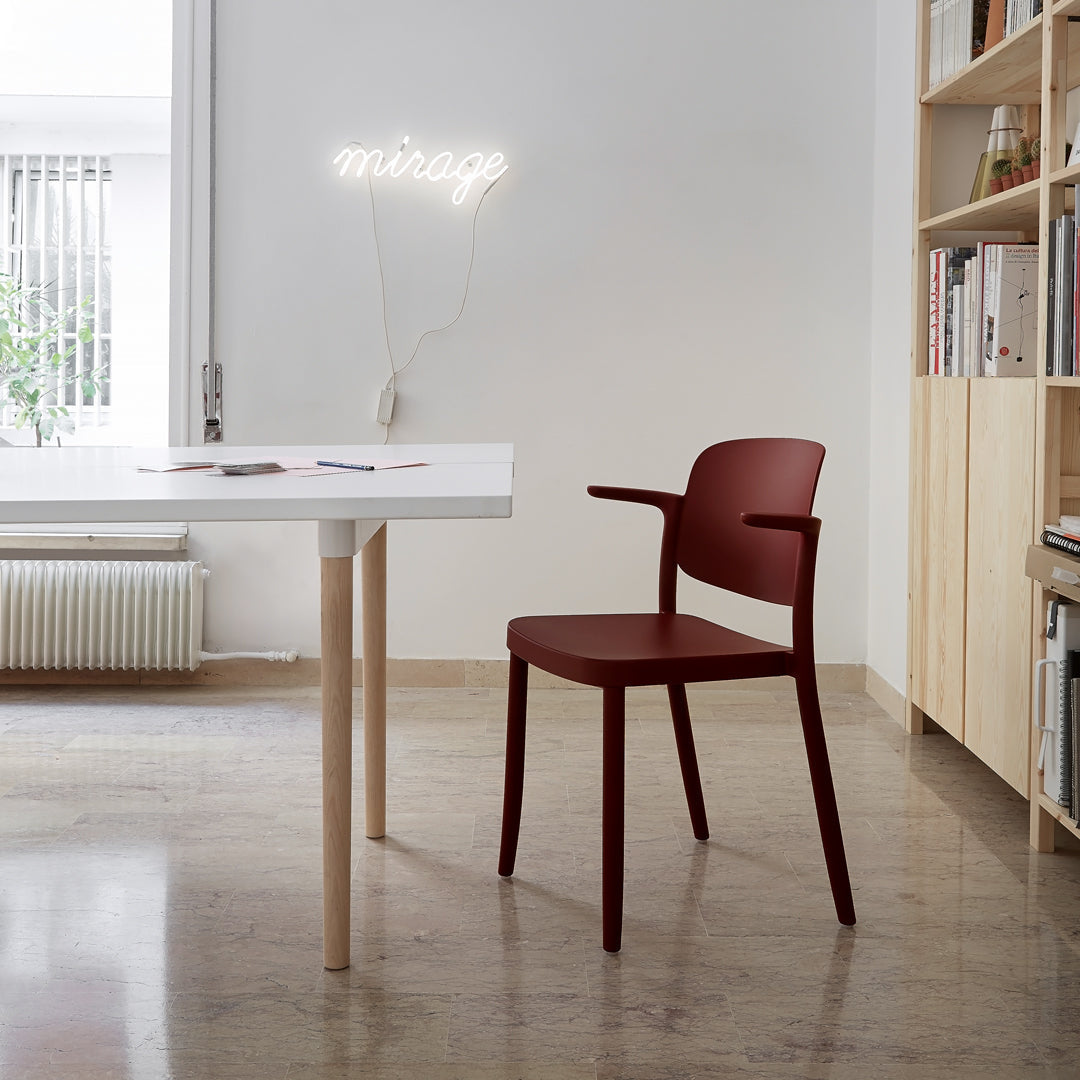 Modern burgundy chair with smooth curves, paired with a minimalist white table and natural wood accents. Bright, neutral room setting.