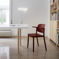 Modern burgundy chair with smooth curves, paired with a minimalist white table and natural wood accents. Bright, neutral room setting.