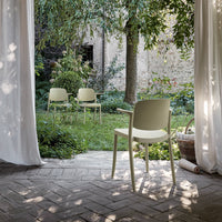 Pale green chairs set against a natural garden backdrop with soft white curtains and textured brick flooring.