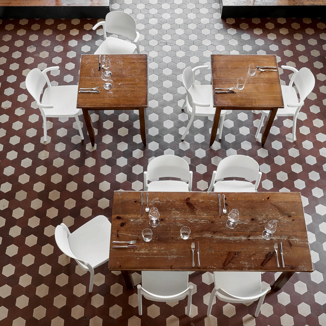 Wooden tables with white chairs on a geometric patterned brown and cream tiled floor.