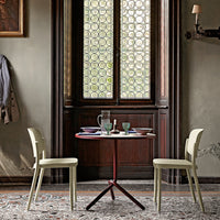 "Light green chairs with round red table, set against a patterned rug and intricate window design."
