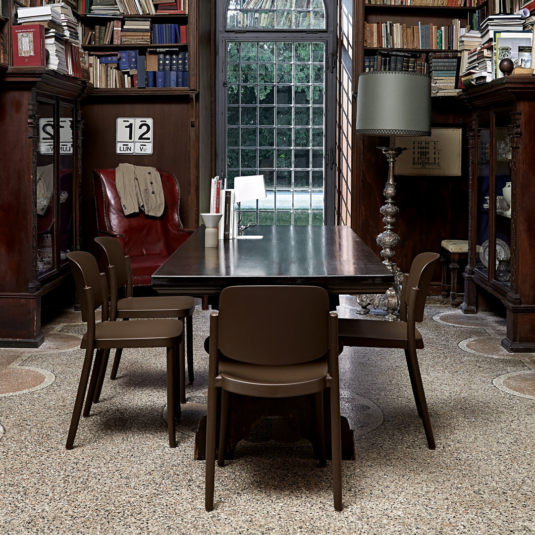Brown dining table with matching chairs in a classic library setting, featuring warm wood tones and intricate floor patterns.