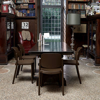 Brown dining table with matching chairs in a classic library setting, featuring warm wood tones and intricate floor patterns.