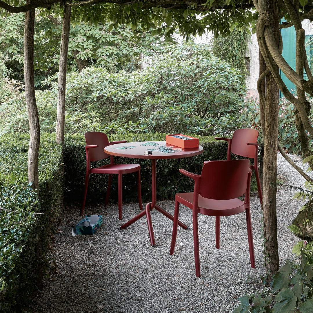 Red outdoor chairs and table set against lush greenery and gravel landscape. Elegant and modern design with solid colors.