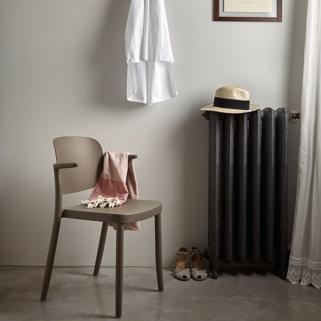 Stylish taupe chair with a soft pink throw, contrasted by dark gray radiator and light wall for a modern look.
