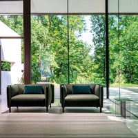 Stylish green armchairs with blue cushions, set against a backdrop of large windows and natural greenery.