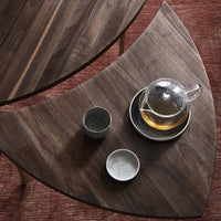 Dark wood table with curved edges, featuring rich grain patterns; grey and white ceramic teacups on a contrasting surface.