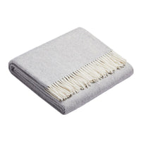 Folded gray blanket with a herringbone pattern and cream fringe trim. Soft texture for cozy warmth.
