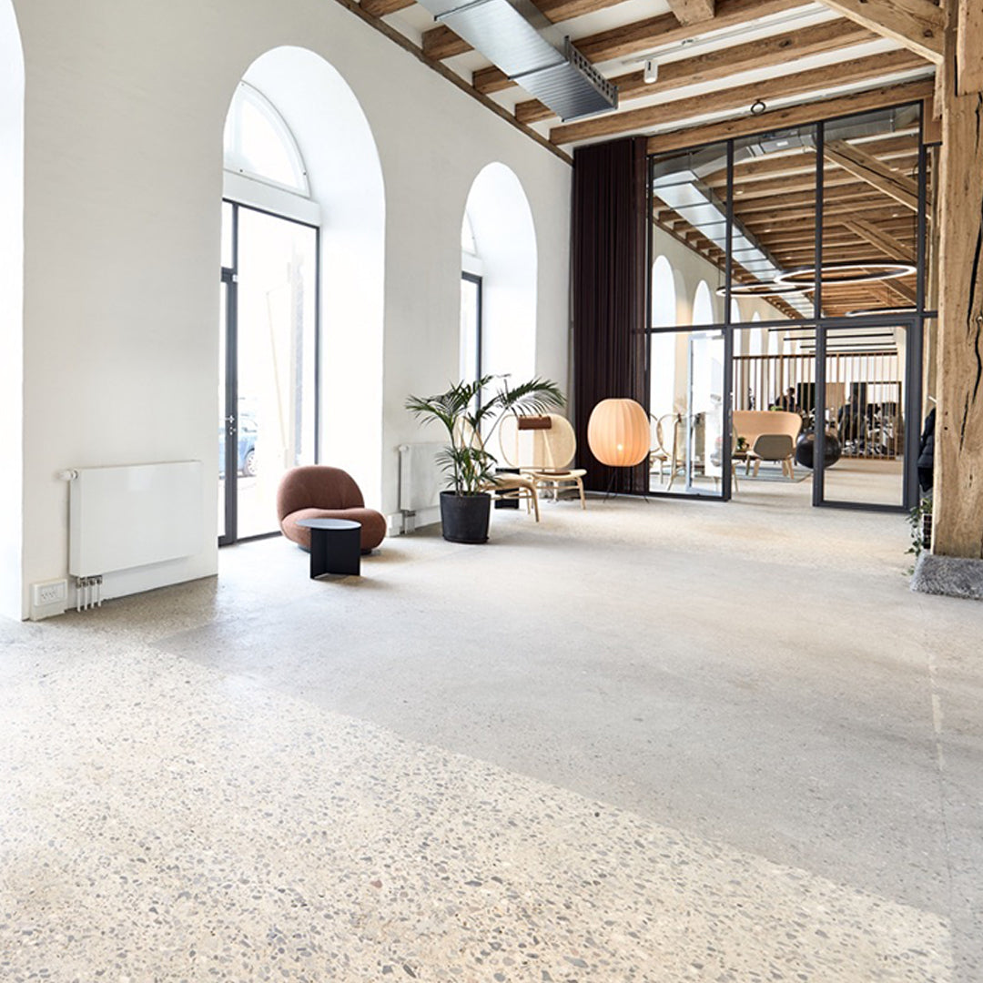 Modern interior featuring neutral tones, wooden beams, and a textured, speckled floor pattern. Bright and airy atmosphere.