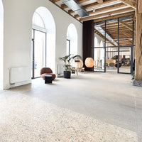 Modern interior featuring neutral tones, wooden beams, and a textured, speckled floor pattern. Bright and airy atmosphere.
