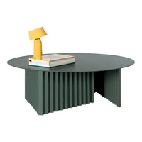 Green round coffee table with ridged base, featuring a yellow lamp and colorful book on top. Modern design, vibrant colors.