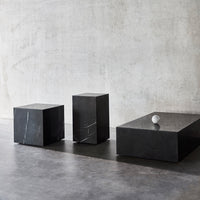 Black marble coffee tables with white veining, featuring modern geometric shapes against a concrete backdrop.