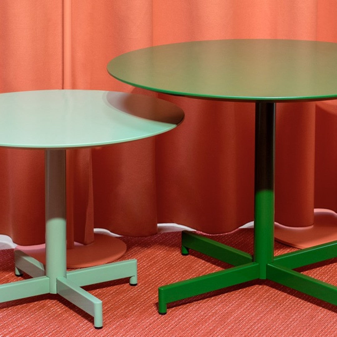 Two round tables in soft green and deep green, against a coral backdrop, on a textured red floor.