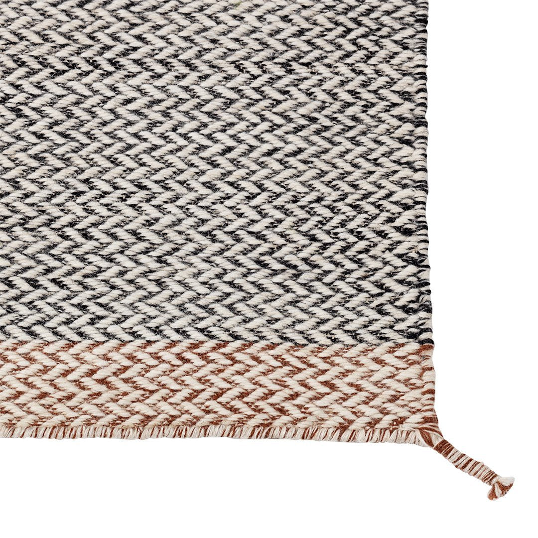 Woven rug featuring a chic black, white, and terracotta herringbone pattern with fringed edges.