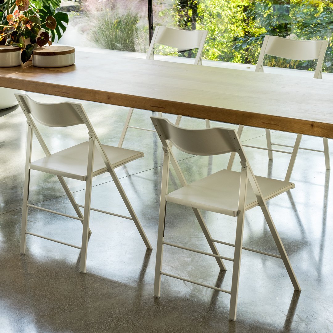 White folding chairs with a minimalist design set against a wooden table in a bright, modern space.