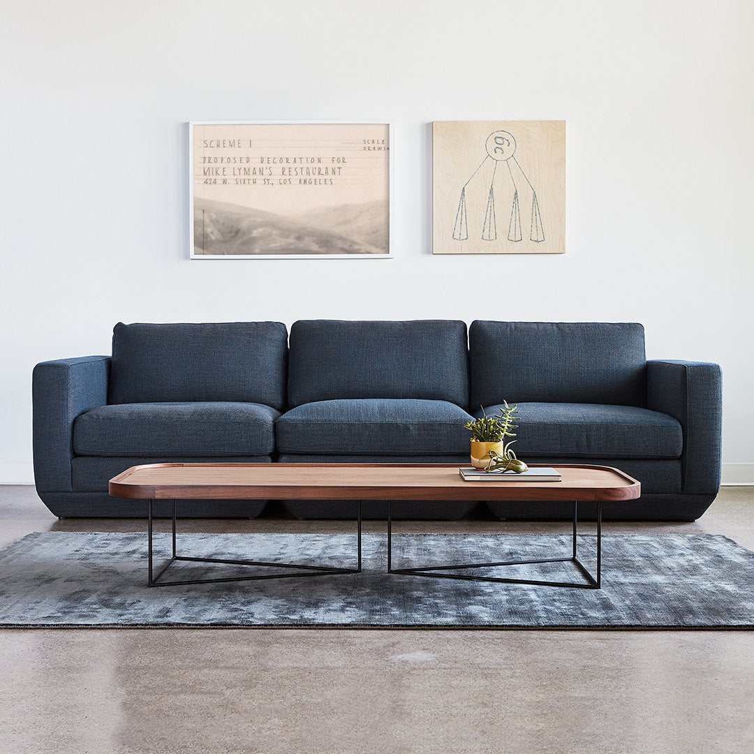 Navy blue sofa with a smooth texture, paired with a wooden coffee table on a gray patterned rug.
