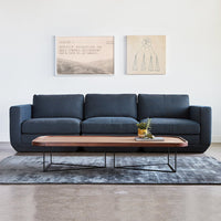 Navy blue sofa with a smooth texture, paired with a wooden coffee table on a gray patterned rug.