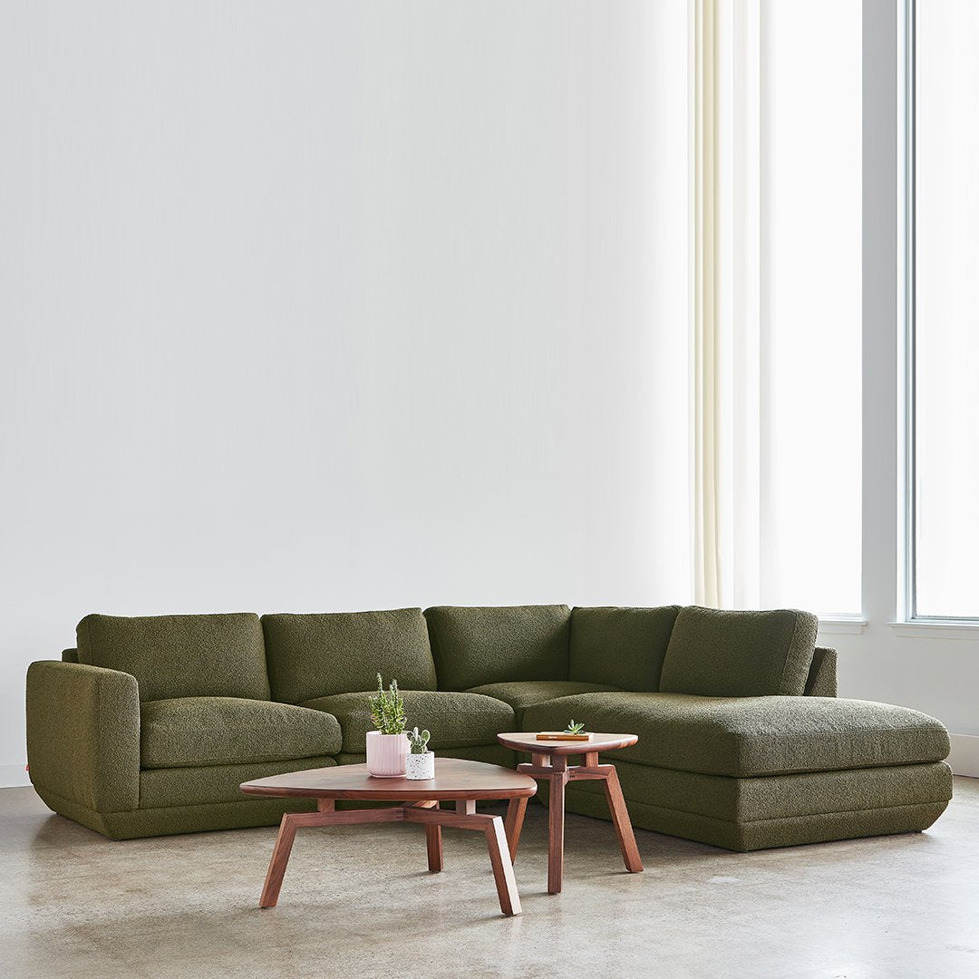 Dark olive green sectional sofa with a textured fabric, paired with light wooden tables.