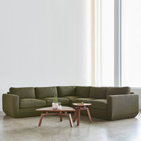 Olive green sectional sofa with smooth fabric; paired with minimalist wooden coffee tables. Bright, modern interior setting.