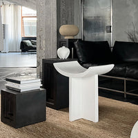 Stylish white accent table with smooth curves, set against a minimalist black and beige living room backdrop.