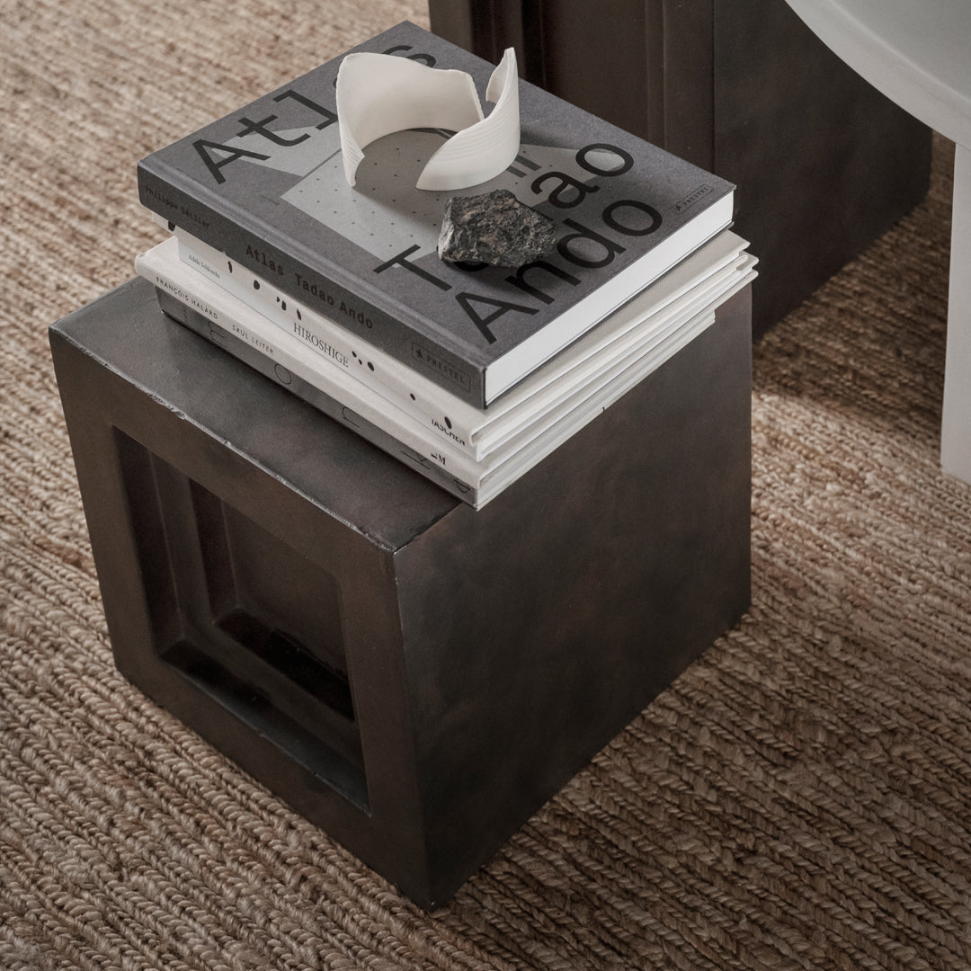 Dark gray cube side table with a smooth matte finish, topped with stacked monochrome books and a decorative object.