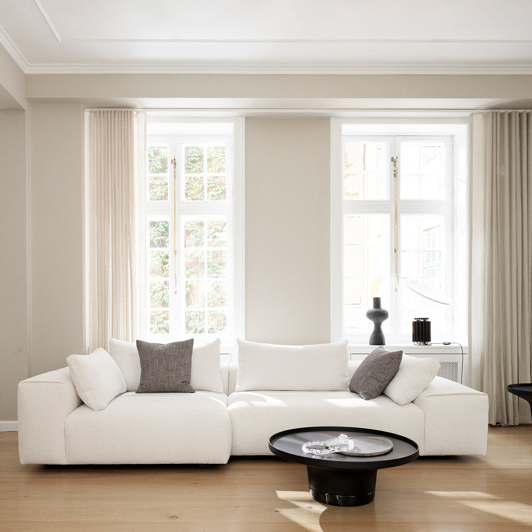 White sectional sofa with gray accent pillows, surrounded by neutral walls and light wood flooring.