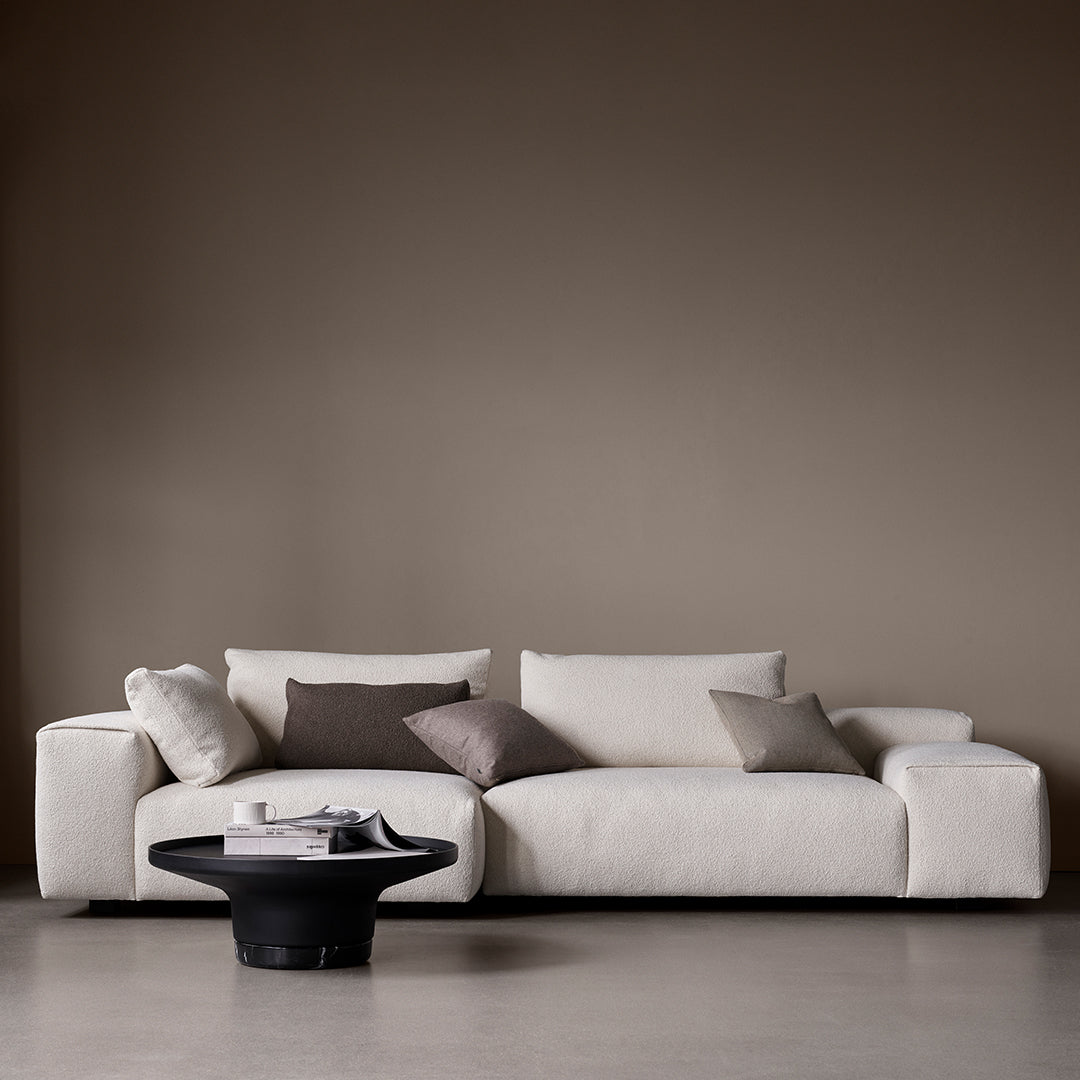 Beige and cream modern sofa with soft textures, accented by dark gray and brown throw pillows. Minimalist design elements.