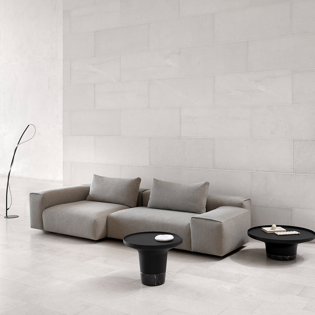 Gray sectional sofa with textured fabric and black tables in a minimalist, neutral-toned setting.