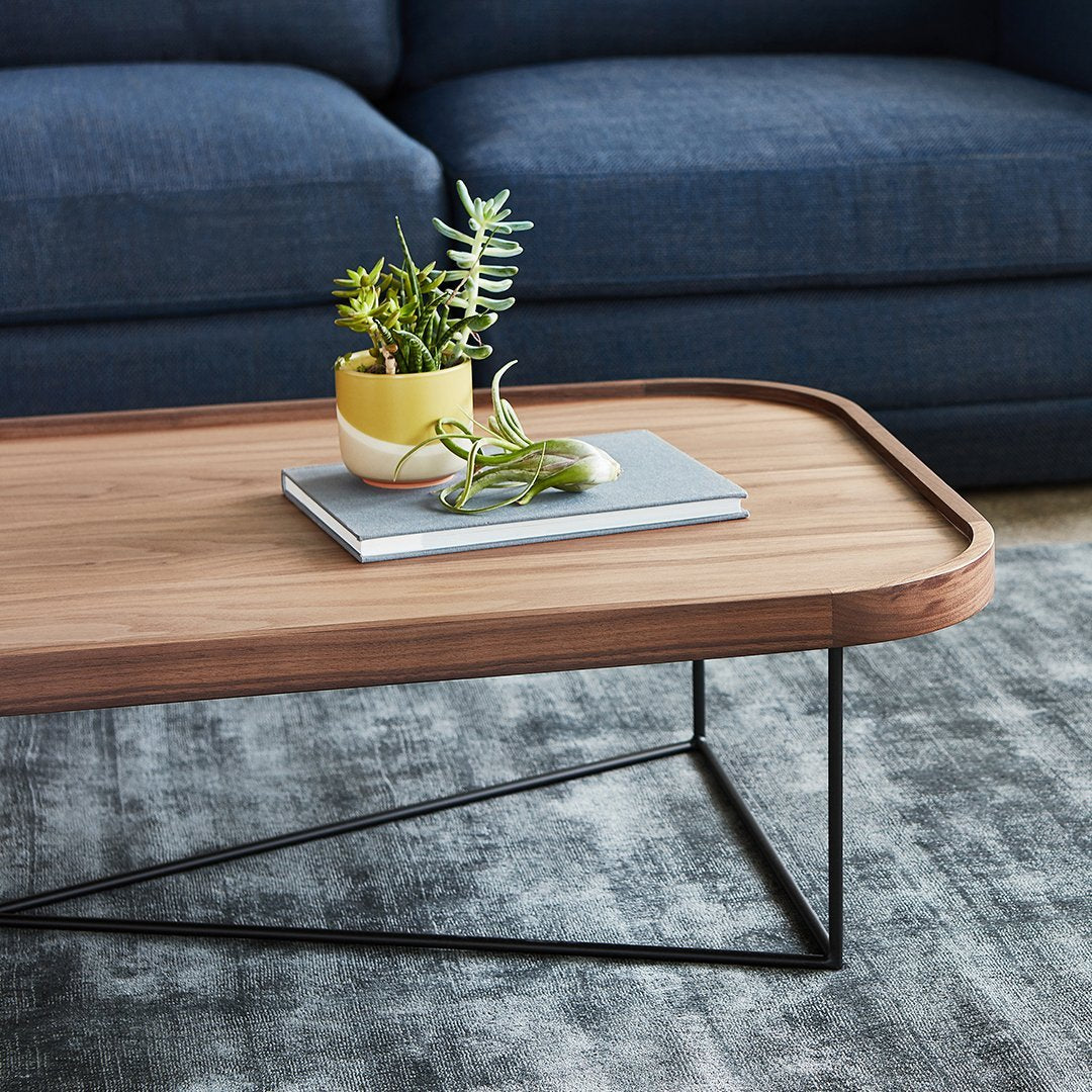 Modern wooden coffee table with a light wood finish and black metal legs, set on a textured gray area rug.